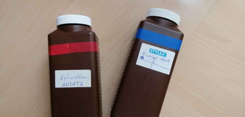 Zwei braune Laborflaschen, eine mit rotem und eine mit blauem Klebeband umwickelt.